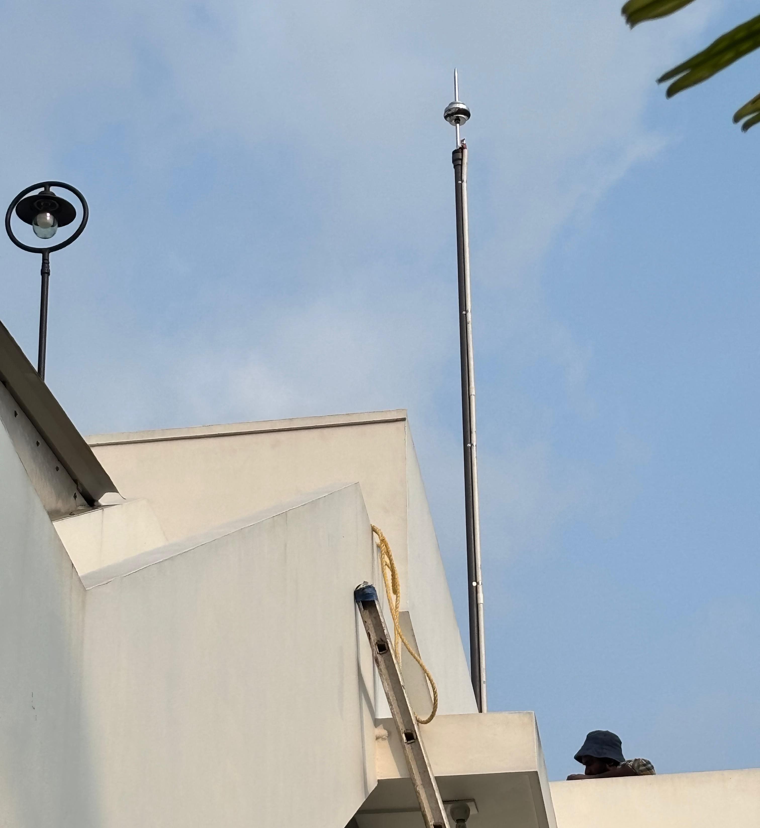 Technician installing a lightning arrester mast on a building rooftop
